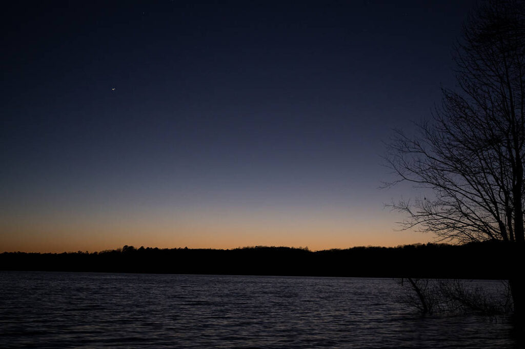 Jupiter, left, and Saturn, right, are seen after sunset above Jordan Lake during the “great conjunction” where the two planets appear a tenth of a degree apart from one another, Monday, Dec. 21, 2020, near Chapel Hill, North Carolina. Credit: (NASA/Bill Ingalls)